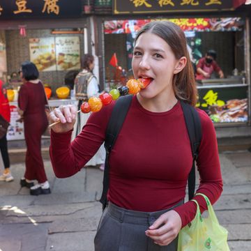 A first-time traveler walking through a traditional Chinese old town street, eating Tanghulu