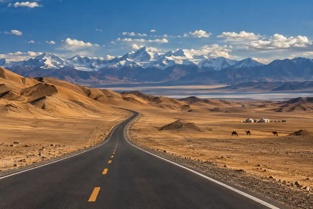Vast northwest China landscape with desert highway, mountains, yurts and camels